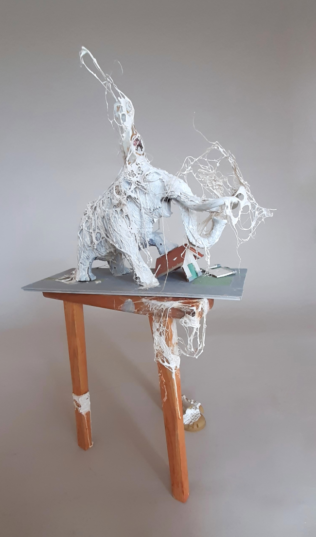 Temps éléphant ou Jumbo time, sculpture contemporaine de Piet.sO - est composée d’un jouet en forme d’éléphant ou mammouth semblant écraser une maison miniature, la tablette qui les accueille est posée sur un tabouret à trois pattes dont l’une est munie d’une sandalette d’enfant nappée de cristaux de sel. En référence à l’actualité, cette pièce fait référence à la brièveté brutale du temps de la destruction, souvent inversement proportionnelle à la durée de construction. Le temps sculpteur peut être exterminateur et détruire à des points de non-retour. L’éléphant fait référence aux éléphants de combat, véritables armes d’assaut de l’Antiquité mêlant la force brute impitoyable à la fascination et aux tyrans contemporains. Exposition, Je t'aime, temps, La Licorne, Saint-Germain-Lembron - 2025