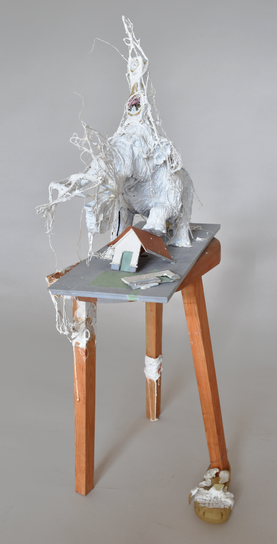 Jumbo time, sculpture contemporaine de Piet.sO - est composée d’un jouet en forme d’éléphant ou mammouth semblant écraser une maison miniature, la tablette qui les accueille est posée sur un tabouret à trois pattes dont l’une est munie d’une sandalette d’enfant nappée de cristaux de sel. 